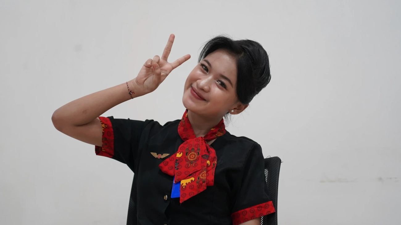 syarat jadi pramugari 2026 Pramugari muda tersenyum menunjukkan tanda damai.